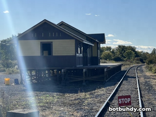 The station set by the tracks with a sun flare and a red STOP sign in front.