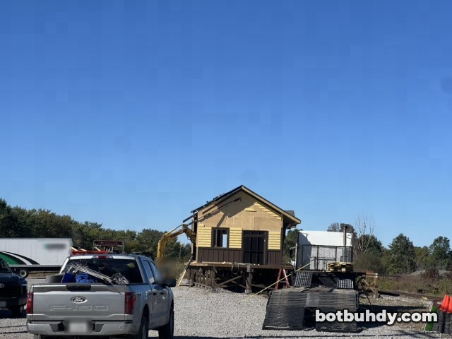 A silver pickup in front of the station, which now has no porch, with an excavator beside it.