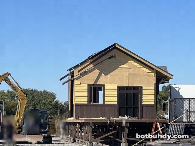 The station front without its porch, an excavator at left and blurred workers nearby.