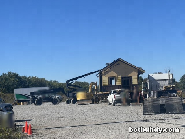 Wide view of a gravel lot with a lift, an excavator, a white pickup and the station behind.