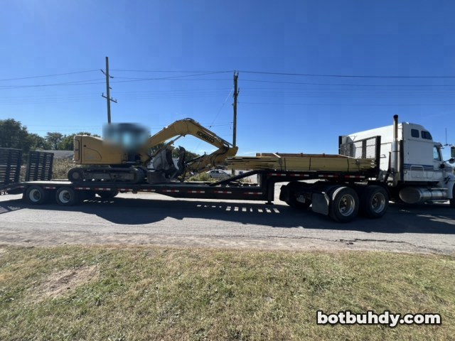 A yellow excavator loaded on a flatbed trailer behind a white semi truck.