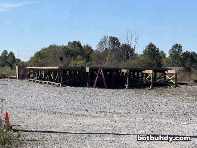 An empty wooden platform frame on a wide gravel lot under a blue sky.