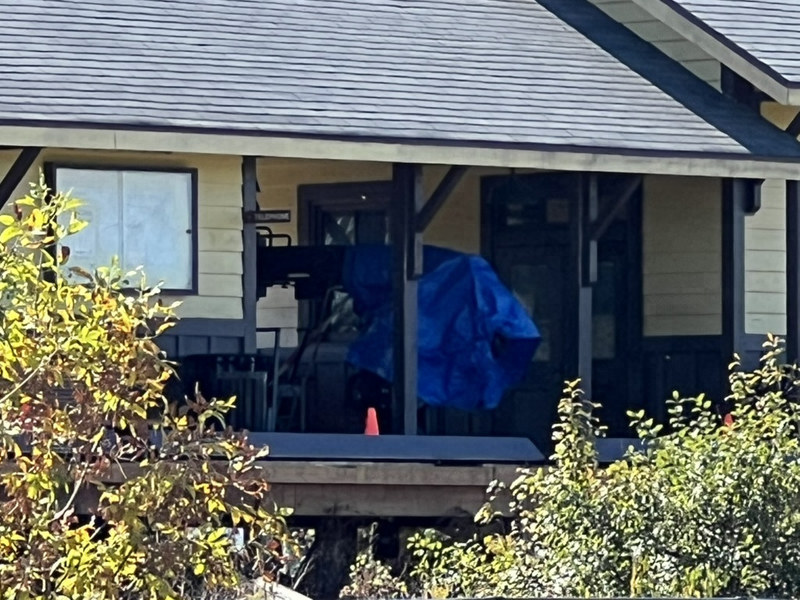 Equipment covered by a blue tarp on the station deck in daylight, with an orange cone and shrubs in front.