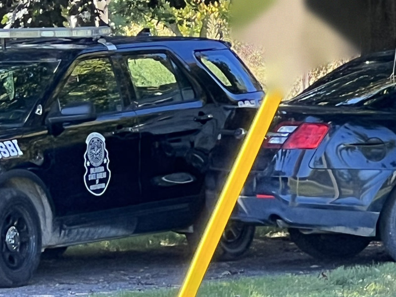 Close view of a black prop SUV with a shield-shaped badge on the door and OSBI on the front fender, beside a dark sedan.