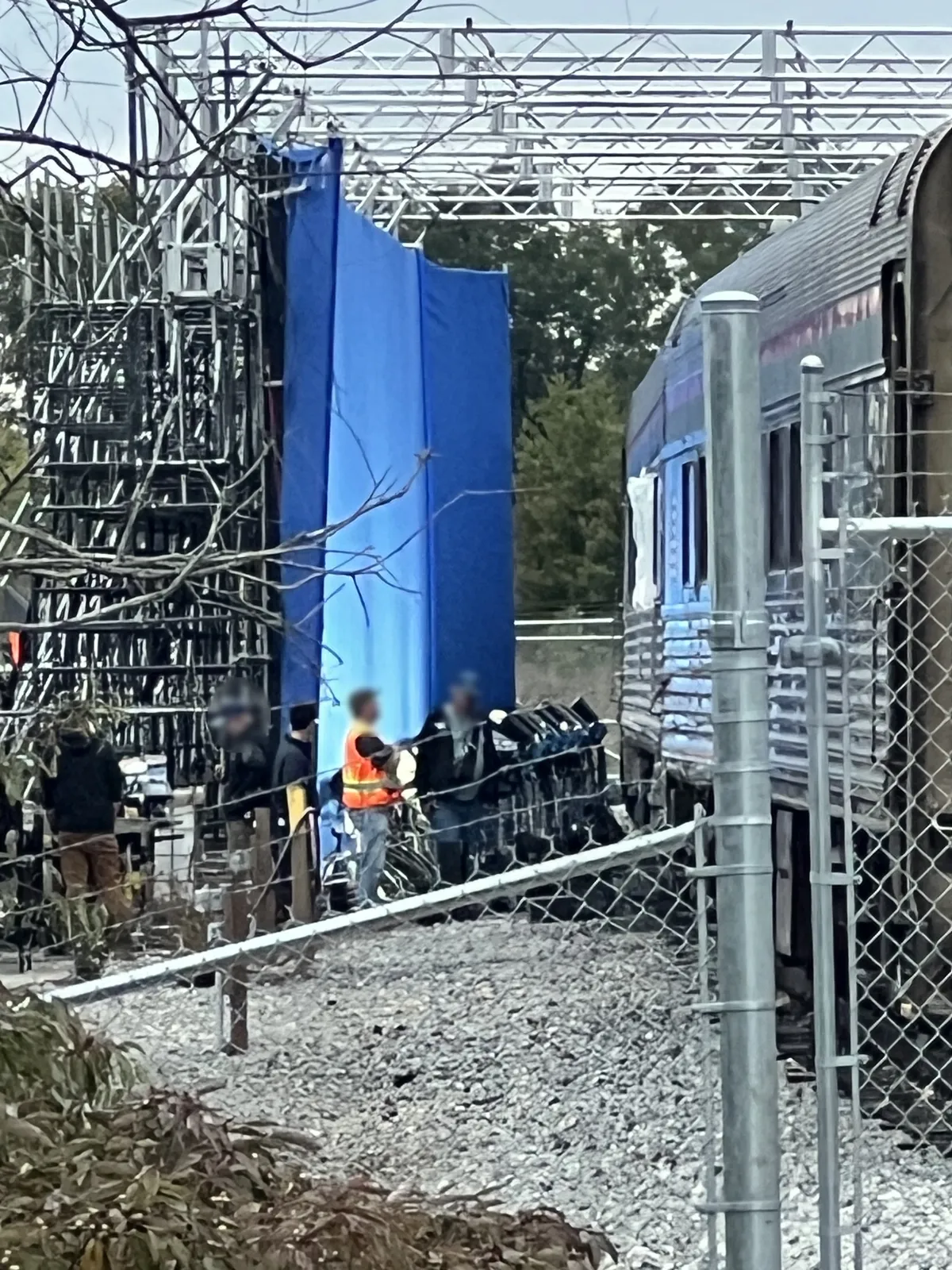 A tall blue screen hanging from scaffolding beside the train car, with a truss grid overhead