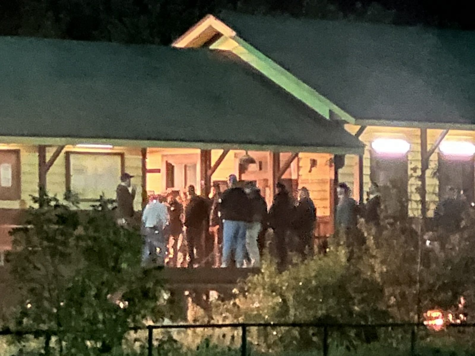 A group of crew standing close together on the lit station deck, seen through bushes from a distance