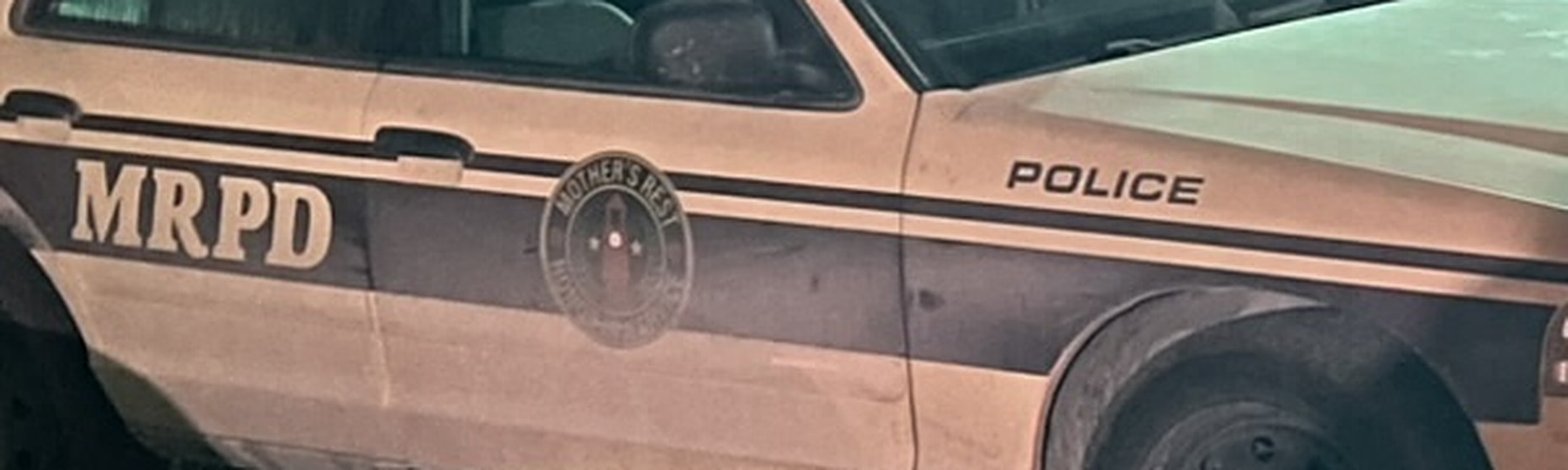 Close-up of the cream police car's side: MRPD in large letters on the rear door, a round seal reading Mother's Rest on the front door, and POLICE on the front fender.